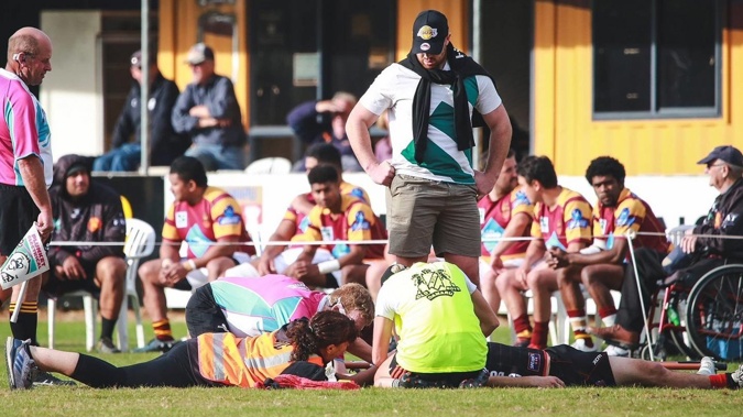 Old Boys fullback Logan Wilson is helped by people including physiotherapists Kerry Whitburn (lying, at left) and Philippa Masoe (in yellow). (Photo / Rebecca Ryan)