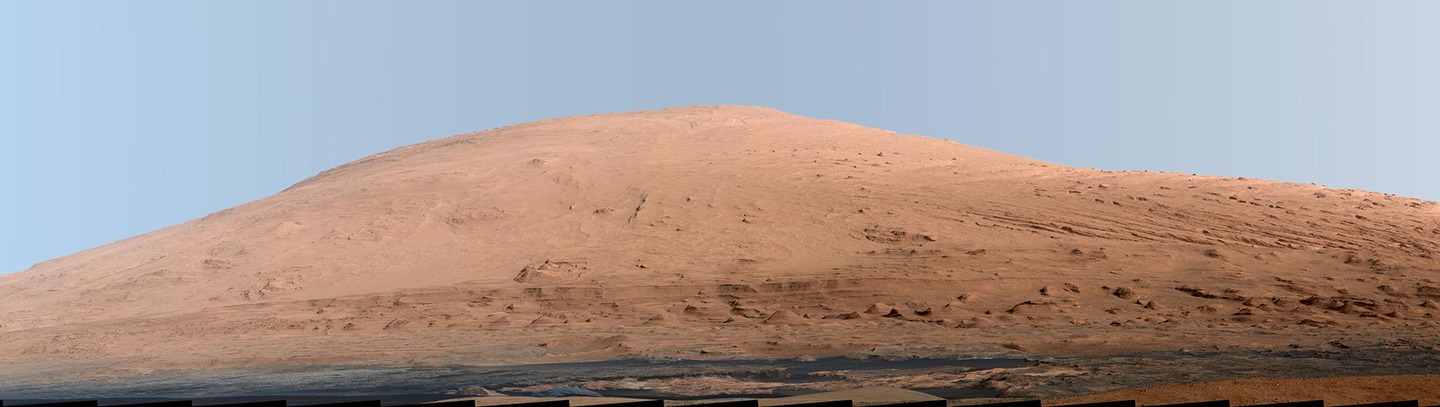 This mosaic of images shows Mount Sharp. White-balanced color adjustment has made the sky look overly blue but shows the terrain as if under Earth-like lighting.
