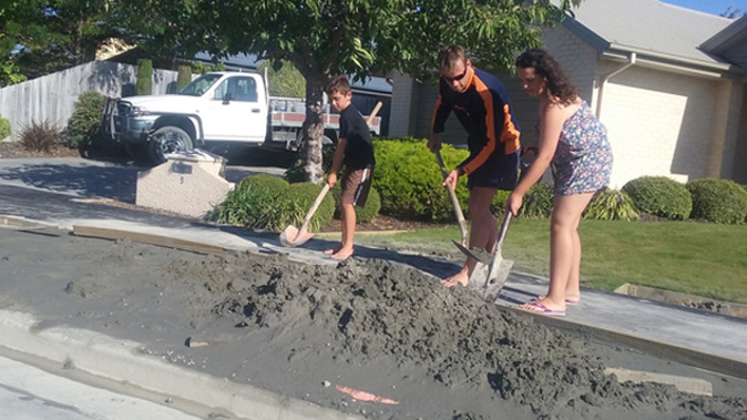 Shane McCarthy shovels liquefaction from outside his Parklands house with his children, Nico, 7, and Chloe, 10 , after yesterday's earthquake in Christchurch. (Kurt Bayer)