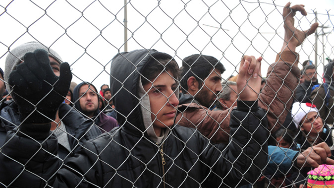 A migrant looks through a fence during a protest in front of anti-riot police at the Greek-Macedonian border, near the Greek village of Idomeni (Getty Images).
