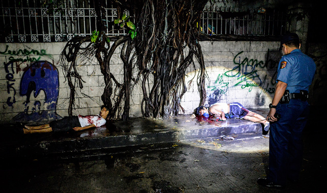 A police officer looks at the corpses of suspected drug pushers who were shot dead following a police operation in Manila (Getty Images) 