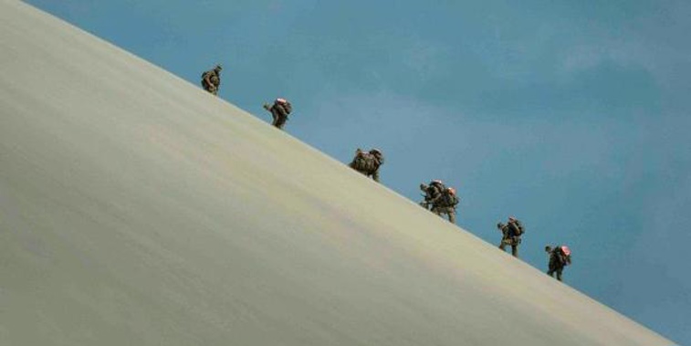 NZSAS candidates scaling a sand dune under 35kg packs carrying 20kg fuel cans (Supplied) 