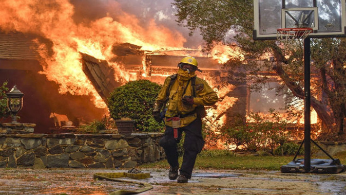 Firefighters work to extinguish a fire at a home as they battle a wildfire in Anaheim Hills. (Photo: NZ Herald/AP)