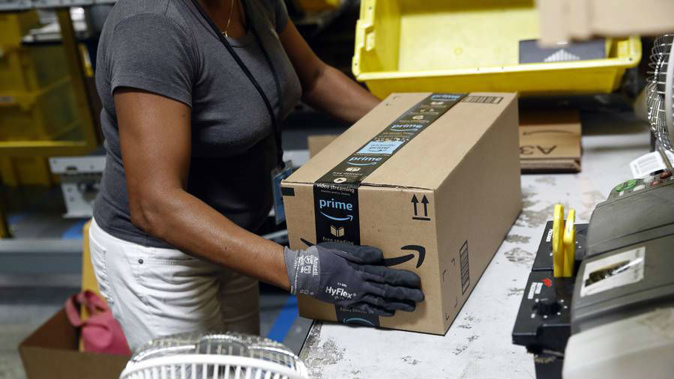 Worker at an Amazon fulfillment centre in Baltimore applies tape to a package before shipment. Labour will be bringing in GST on goods bought online. (Photo / AP)