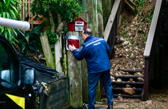 A police officer places a red sticker on a Remuera property after rain causes widespread damage in Auckland. Photo / Alex Burton