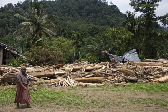 A woman walks near logs swept into a neighborhood affected by a flash flood in Pesisir Selatan, West Sumatra, Indonesia, Wednesday, March 13, 2024. (AP Photo/Mavendra JR)