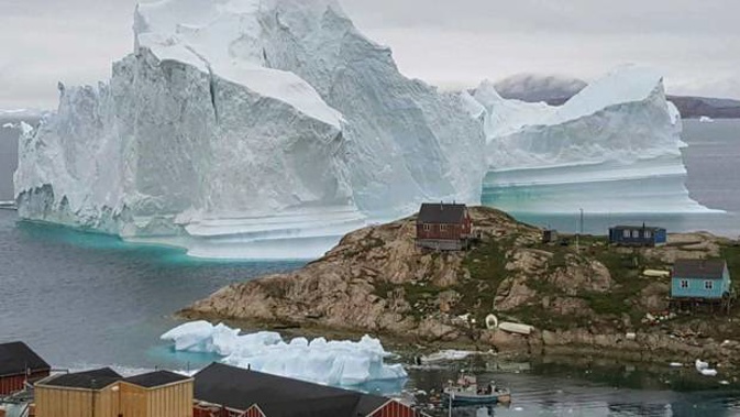 An iceberg towers over the village Innarsuit, on the northwestern Greenlandic coast. (Photo / AP)
