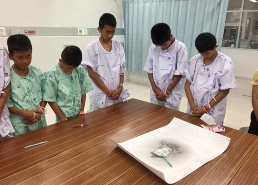 Some of the rescued soccer team members bowing their heads respectfully in front of a sketch of the Thai Navy SEAL diver who died while trying to rescue them. (Photo / AP)