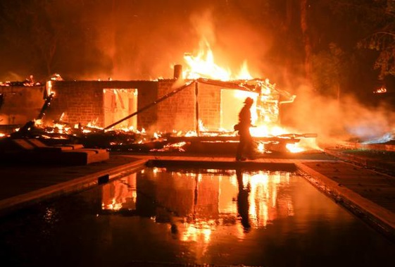 A firefighter walks by the a burning home in Malibu, California, yesterday. (Photo / AP)