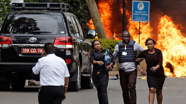 Security forces help civilians flee the scene as cars burn behind them at a hotel complex in Nairobi, Kenya. Photo / AP