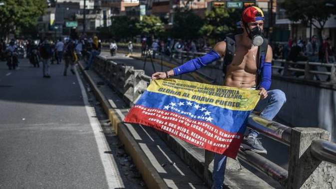 A demonstrator seen holding the Venezuelan flag while wearing a gas mask during a demonstration against President Nicolas Maduro's policies. Photo / Getty Images
