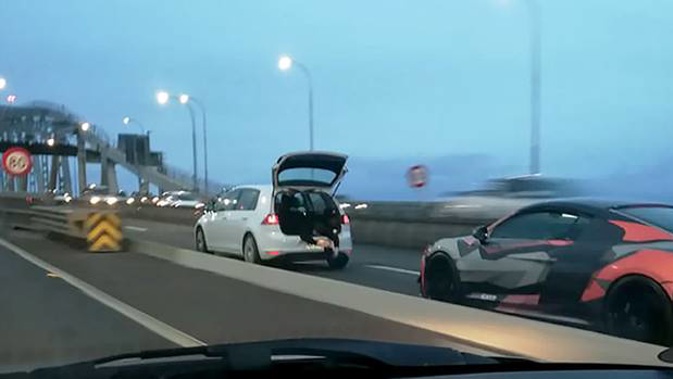 A photographer hangs out of the boot of a moving car (white car with raised tailgate) on the Auckland Harbour Bridge. (Photo / Supplied)