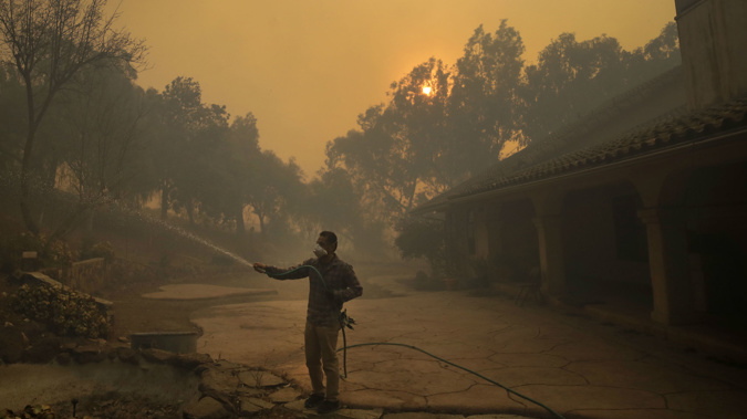 A local uses a hose to protect his girlfriend's house from the approaching fire. (Photo / AP)