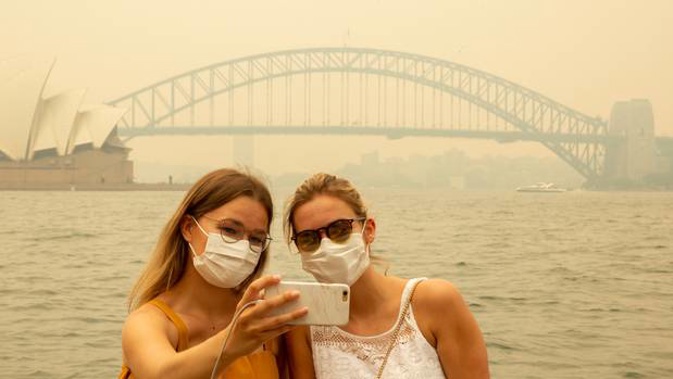 Tourists wearing masks take photos as the Sydney Opera House is enveloped in haze caused by nearby bushfires. Photo / Getty Images