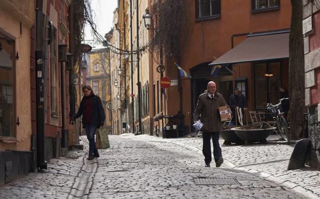 People walk down a quiet cobbled street in Stockholm. The streets are quiet but not deserted.