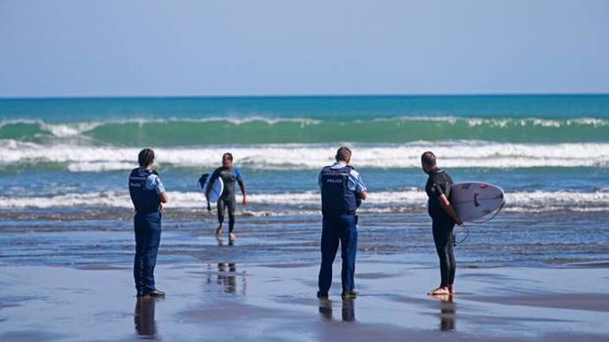 Surfers are spoken to and issued tickets by the police at Piha beach this morning after they breached the lockdown rules. Photo / Alex Burton