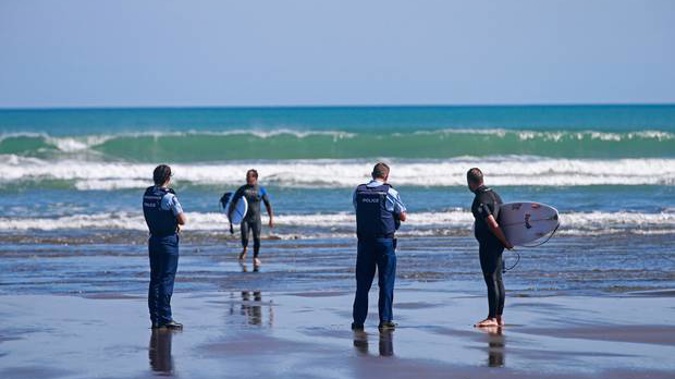 Surfers are spoken to and issued tickets by the police at Piha beach this morning after they breached the lockdown rules. Photo / Alex Burton