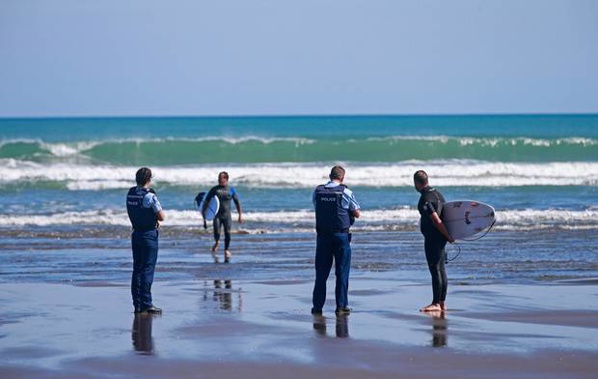 Surfers are spoken to and issued tickets by the police at Piha beach this morning after they breached the lockdown rules. Photo / Alex Burton