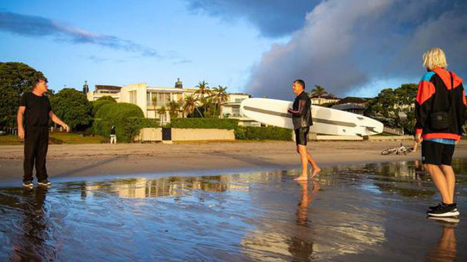 A concerned resident questions a man why he is deliberately flouting lockdown rules by surfing at Takapuna beach this morning. Another young resident, to the right, was spoken to by police yesterday.