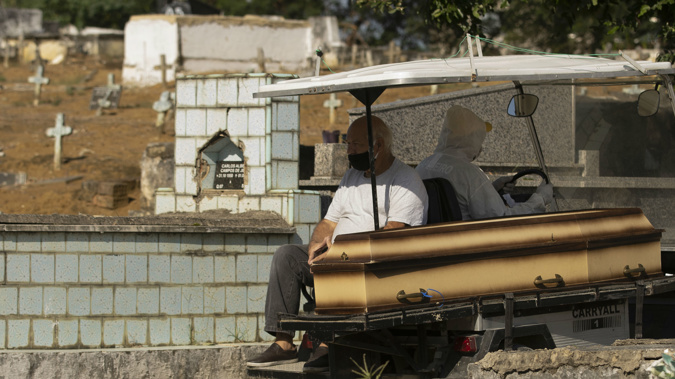 A man wearing a mask sits next the coffin of his mother as he's transported by a cemetery worker in a full protection suit to her burial site at the Nossa Senhora das Gracas cemetery in Duque de Caxias. (Photo / AP)