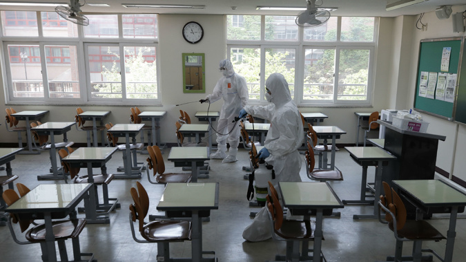 Health officials wearing protective gear spray disinfectant to help reduce the spread the new coronavirus ahead of school reopening in a cafeteria at a high school in Seoul,