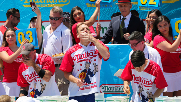 Joey Chestnut (centre) eats during the men's hot dog eating contest on July 4, 2019 in New York City. (Photo / Getty)