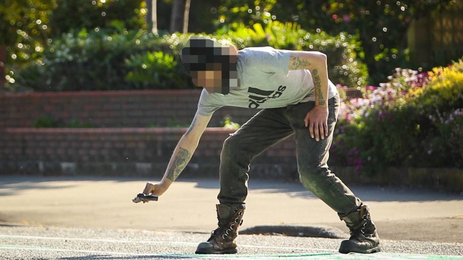 This man yelled out to armed police 'it's not me' before slowly lowering this replica firearm to the road. Another man was arrested shortly after. (Photo / Paul Taylor)