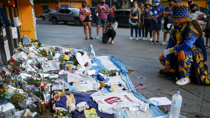 A fan mourns in front of flowers and posters left in tribute to Diego Maradona at the entrance of the Boca Juniors stadium known as La Bombonera in Buenos Aires. (Photo / AP)