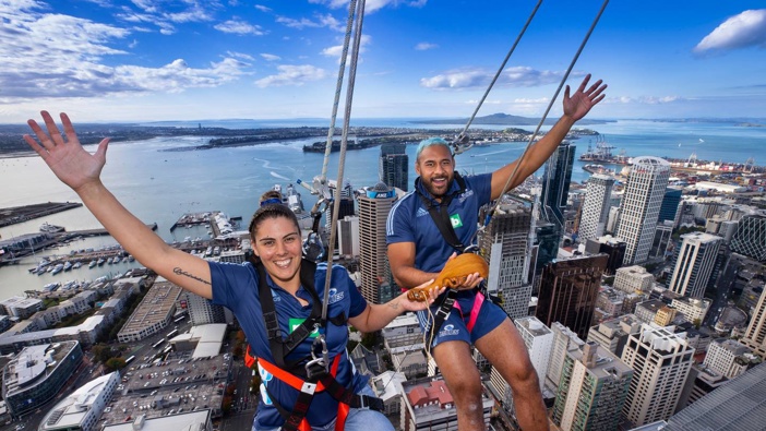 Blues Super Rugby captains Eloise Blackwell and Patrick Tuipulotu hang off the Sky Walk at the Auckland Sky Tower with the women's rugby trophy, the Waipuea Womens Rugby Taonga. (Photo / Brett Phibbs)
