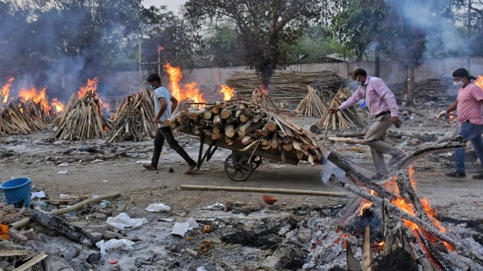 A worker carries wood on a hand cart as multiple funeral pyres of Covid-19 victims burn at a crematorium on the outskirts of New Delhi. (Photo / AP)