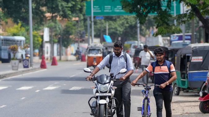 A motorist pushes his motorcycle along with a cyclist amid fuel shortages in Sri Lanka. Photo / Eranga Jayawardena, AP