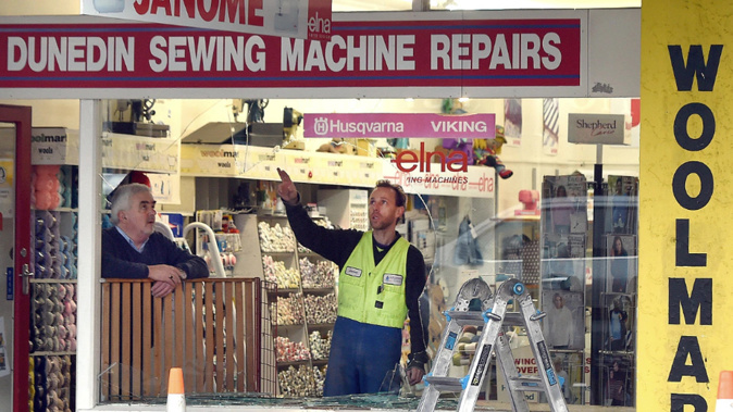 Dunedin Sewing Machine Repairs owner Mike McNulty watches as a glazier assesses his South Dunedin shop window. Photo / Peter McIntosh