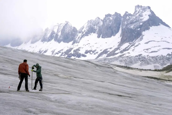 Team members of ETH (Swiss Federal Institute of Technology) glaciologist and head of the Swiss measurement network 'Glamos', Matthias Huss, drill holes into the Rhone Glacier to take measurements near Goms, Switzerland, Friday, June 16, 2023. (AP Photo/Matthias Schrader)