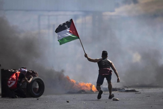 A protester waves the Palestinian flag during clashes with the Israeli forces at the Hawara checkpoint, south of the West Bank city of Nablus. (Photo / AP)