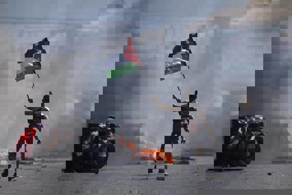A protester waves the Palestinian flag during clashes with the Israeli forces at the Hawara checkpoint, south of the West Bank city of Nablus. (Photo / AP)