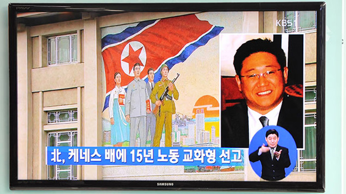 Passersby watch a local television broadcast in Seoul on May 2, 2013 showing a report and picture of Kenneth Bae (R), a Korean-American tour operator detained in North Korea, against the background of a North Korean flag painted on the wall of a building in Pyongyang. (Getty)