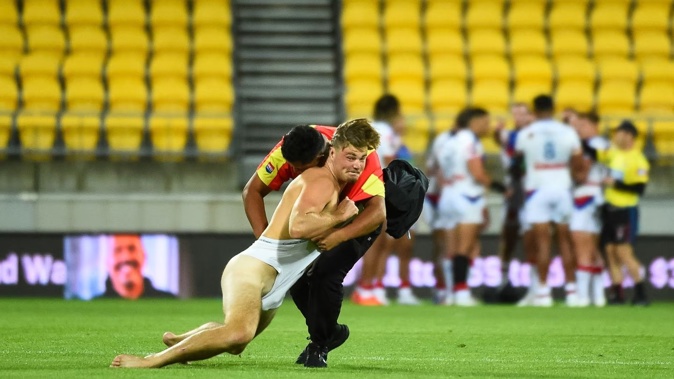 A pitch invader is tackled to the ground during the Warriors' victory over the Knights at Sky Stadium. Photo / Photosport