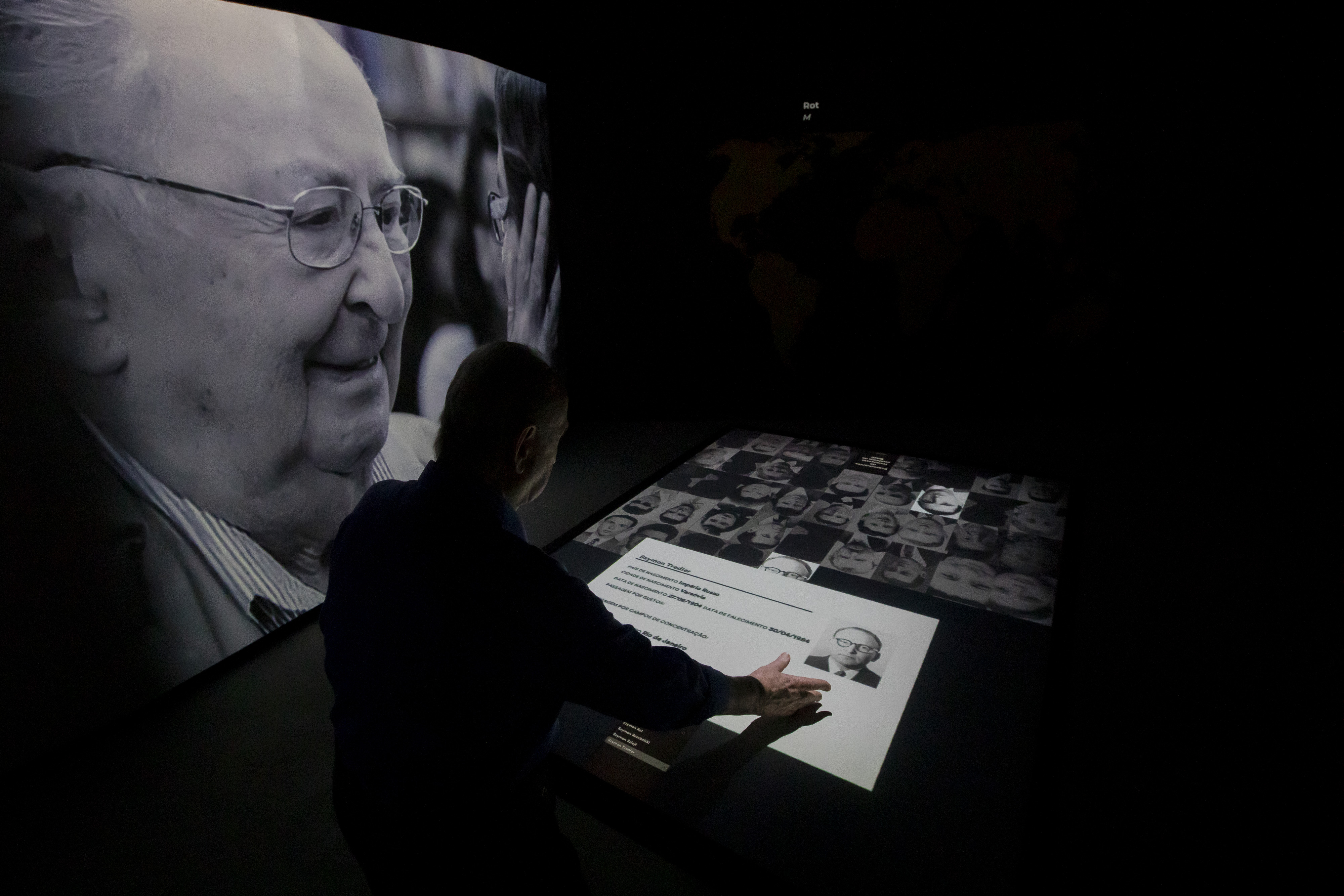 Jorge Tredler, 83, of Poland, who came to Brazil with his family in Feb. 1951 after taking refuge in Russia and other countries during the second World War, points to a photo of his father Szymon on an interactive table that tells the stories of thousands of people who took refuge in Brazil during the Holocaust, at the Holocaust Victims Memorial on its opening day to the public in Rio de Janeiro, Brazil, Thursday, Jan. 19, 2023. Another photo of his father is displayed at left. Photo / AP