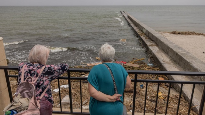 People look at a polluted beach with objects some of which presumably were washed down the Dnipro River as the result of the Kakhovka dam destruction on June 13, 2023 in Odesa, Ukraine.