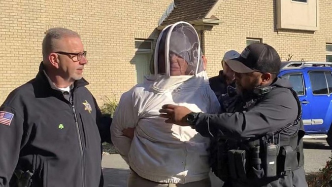 Rorie S Woods wears a beekeeping suit while taken into custody. Photo / AP