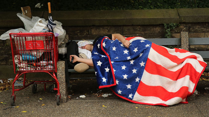 A homeless man sleeps under an American Flag blanket on a park bench on September 10, 2013 in the Brooklyn borough of New York City (Getty Images)