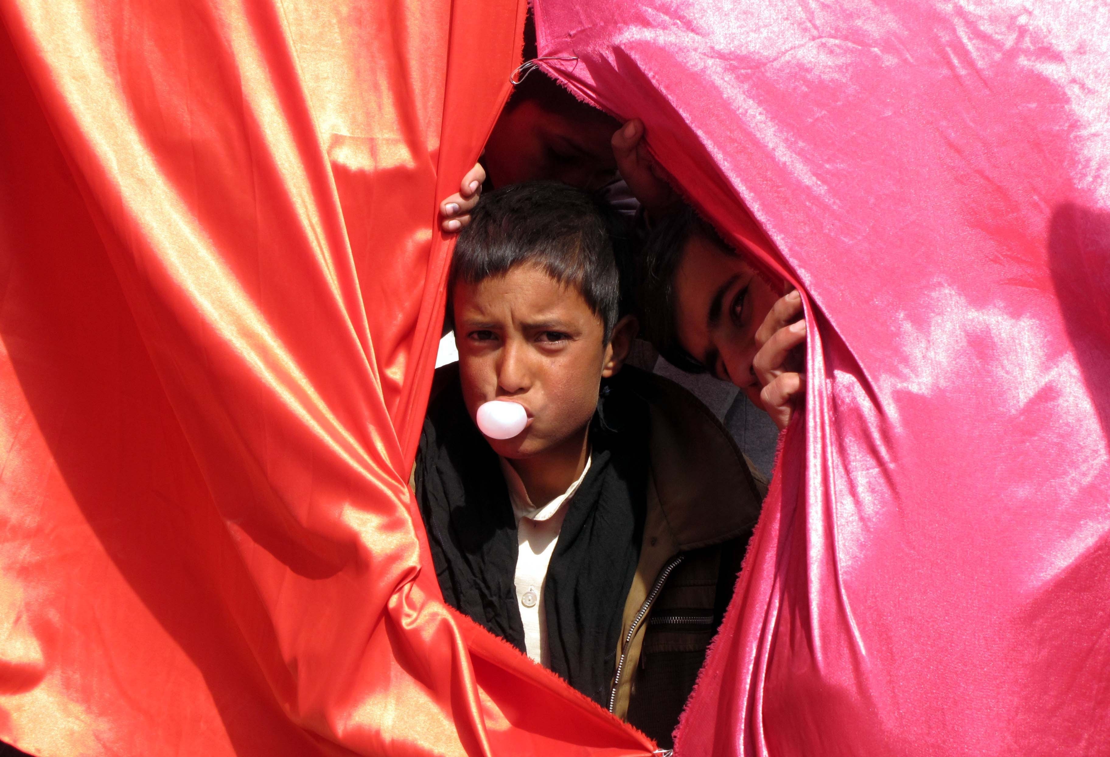 An internally displaced Afghan child blows bubble gum as the children prepare to attend a graduation ceremony organized by the Mobile Mini Circus for Children in Kabul, Afghanistan. 