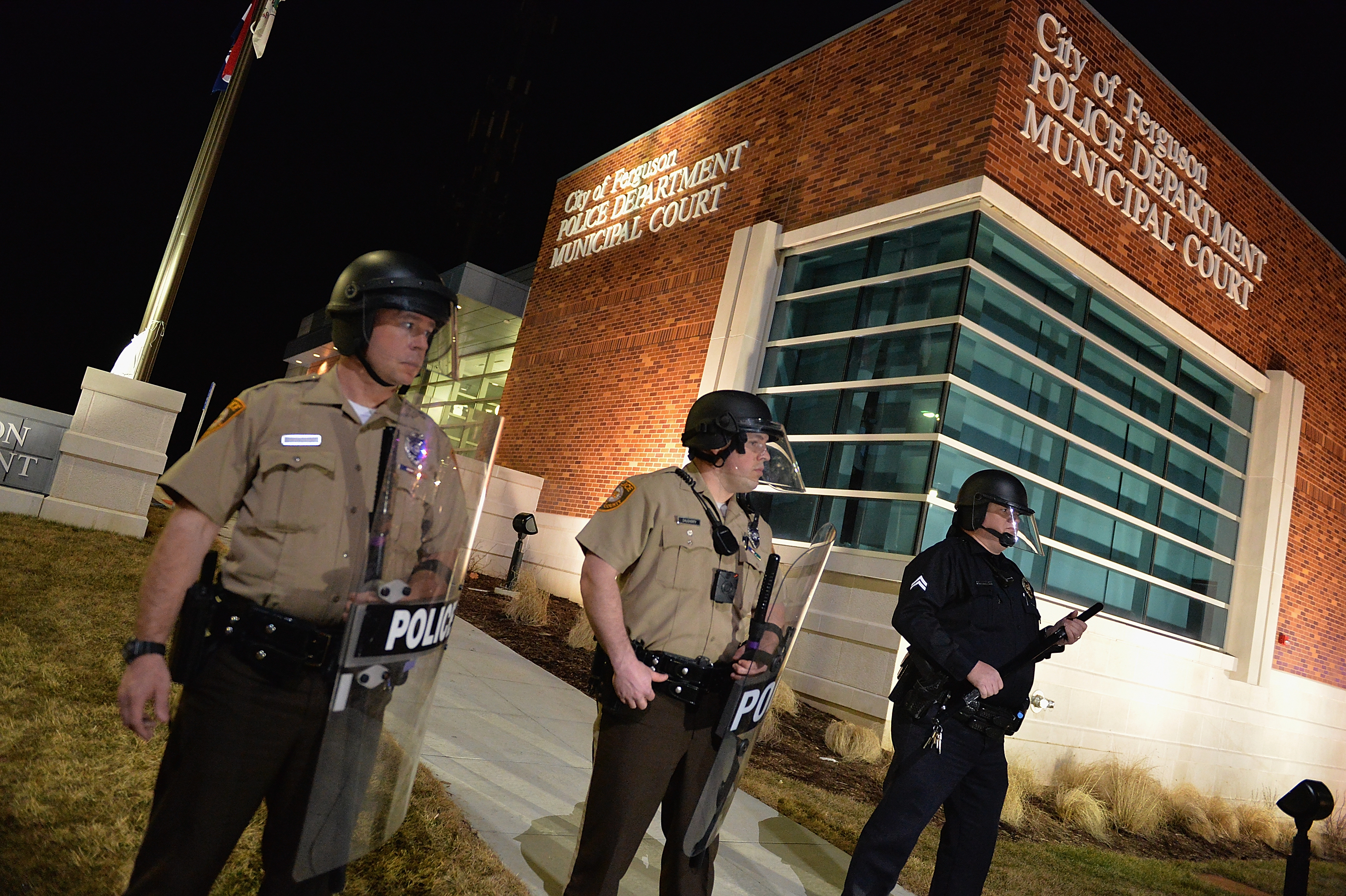 Police in riot gear stand guard outside the Ferguson Police Station. 