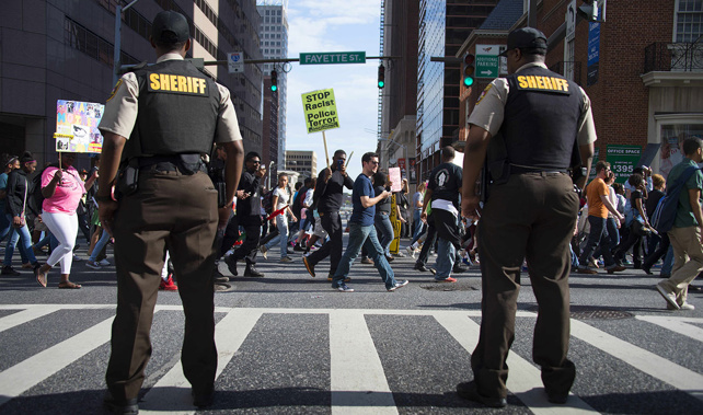 Police stand watch as demonstrators march through the streets in Baltimore (Getty Images) 