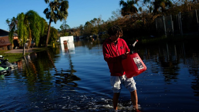 Jose Cruz, 13, carries an empty Jerrycan through receding flood waters outside his house as his family heads out to look for supplies, three days after the passage of Hurricane Ian, in Fort Myers, Florida. Photo / AP