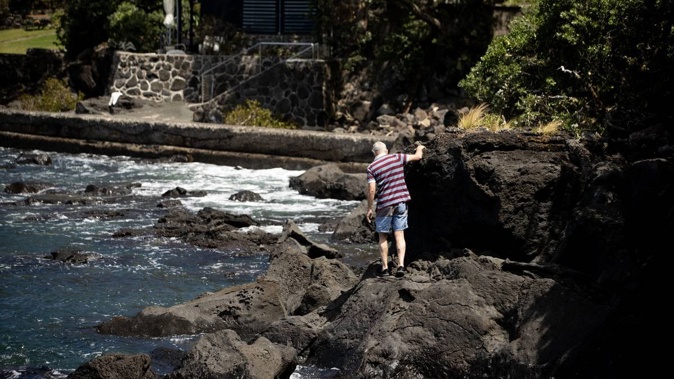 A man tries to negotiate the rocks around part of the Takapuna-Milford walkway after a track through private property was closed because of a dispute with Auckland Council. Photo / Dean Purcell