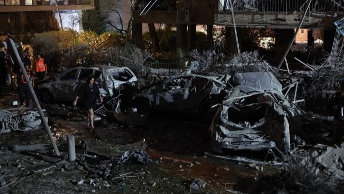 A woman walks between charred cars in front of a building hit by a missile fired from Iran, in Ramat Gan near Tel Aviv. Photo / Jack Guez, AFP