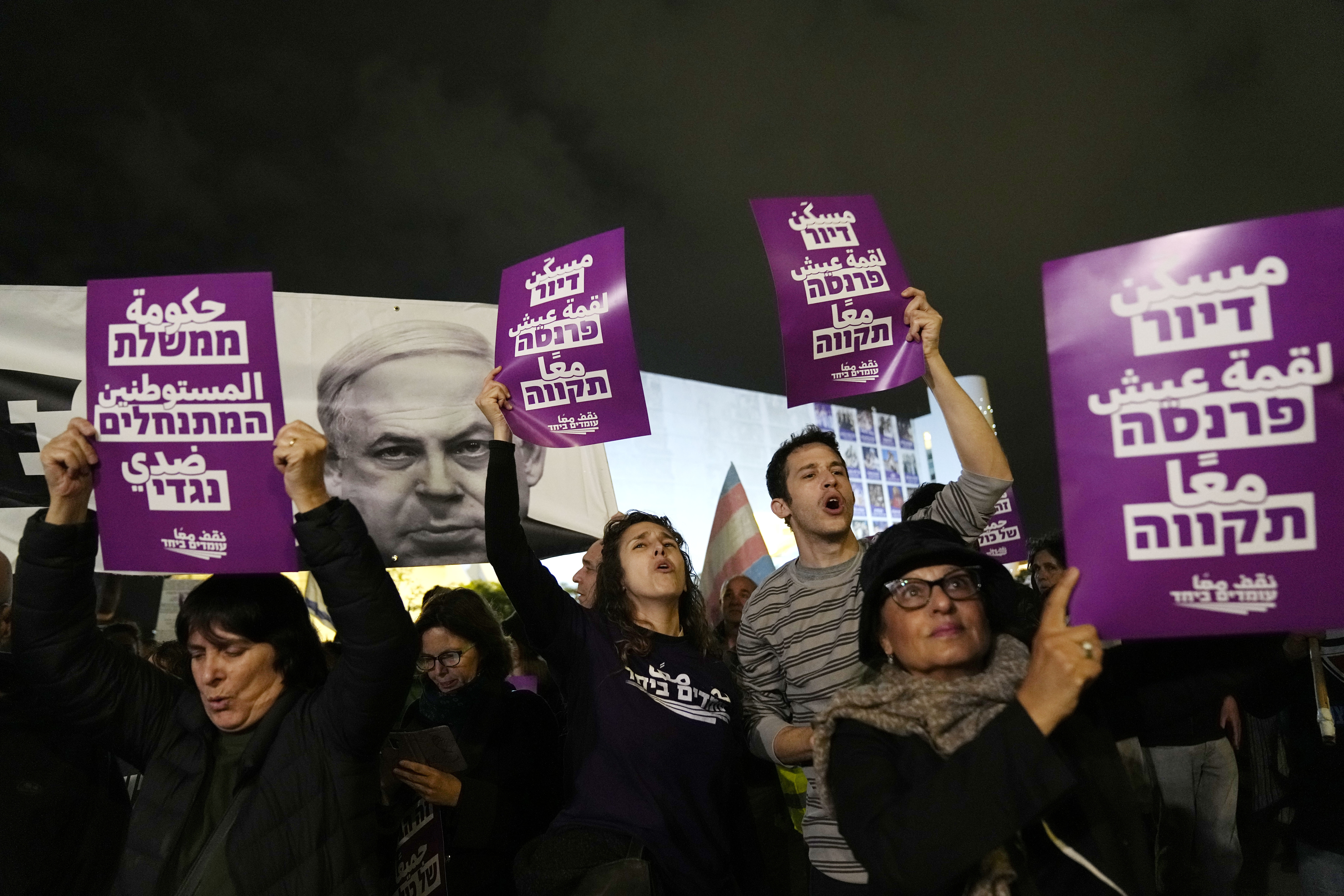 Activists chant slogans in Tel Aviv, Israel, to protest against Prime Minister Benjamin Netanyahu's far-right government, Saturday, Jan. 7, 2023. The placard at left reads: "The settler government is against me."; the placard at right reads: "housing, livelihood, hope." Photo / AP