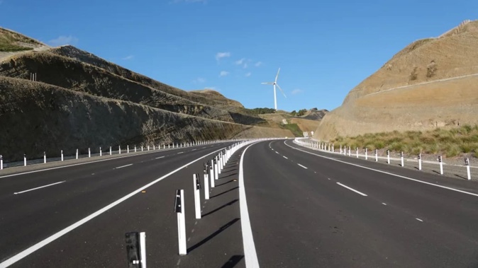 The four-lane highway snakes through hills and between wind turbines. Photo / RNZ