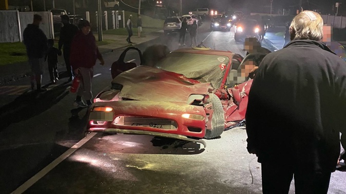 Residents crowd around the car shortly after it had crashed into a power pole and caught fire on Pah Rd in Cockle Bay on Friday. Photo / Supplied